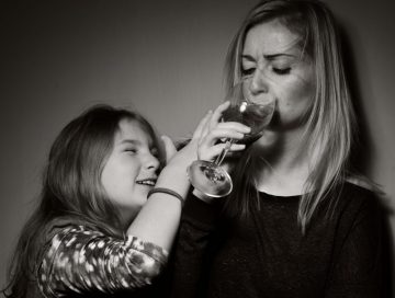 A young girl trying to keep her mother from drinking a glass of wine